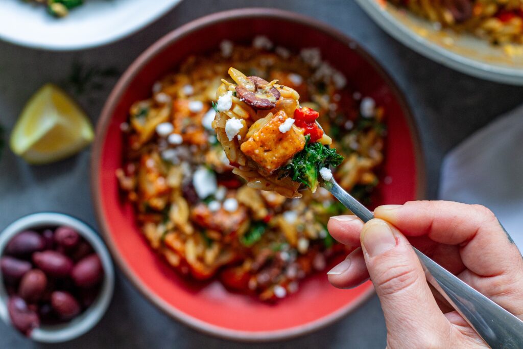 A serving of creamy orzo topped with tofu, vegan cheese, and fresh herbs.