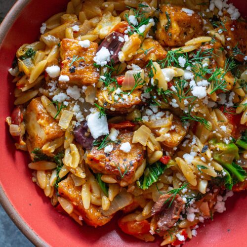 A serving of creamy orzo topped with tofu, vegan cheese, and fresh herbs.