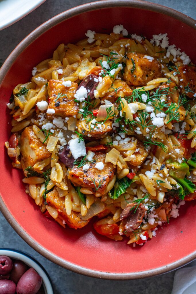 A serving of creamy orzo topped with tofu, vegan cheese, and fresh herbs.