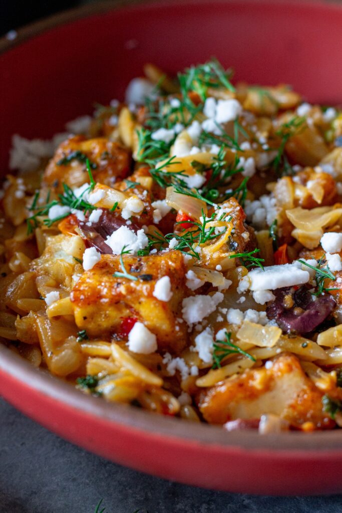 A serving of creamy orzo topped with tofu, vegan cheese, and fresh herbs.