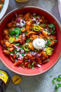 A bowl of cheesy and hearty One-Pot Lentil Chili Mac topped with fresh cilantro, red onion, pickled jalapeño, and vegan sour cream.