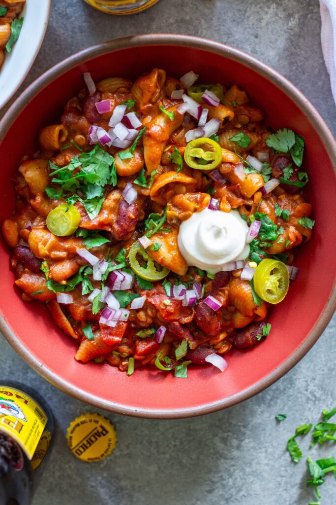 A bowl of cheesy and hearty One-Pot Lentil Chili Mac topped with fresh cilantro, red onion, pickled jalapeño, and vegan sour cream.