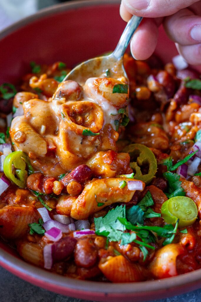 A bowl of cheesy and hearty One-Pot Lentil Chili Mac topped with fresh cilantro, red onion, pickled jalapeño, and vegan sour cream.