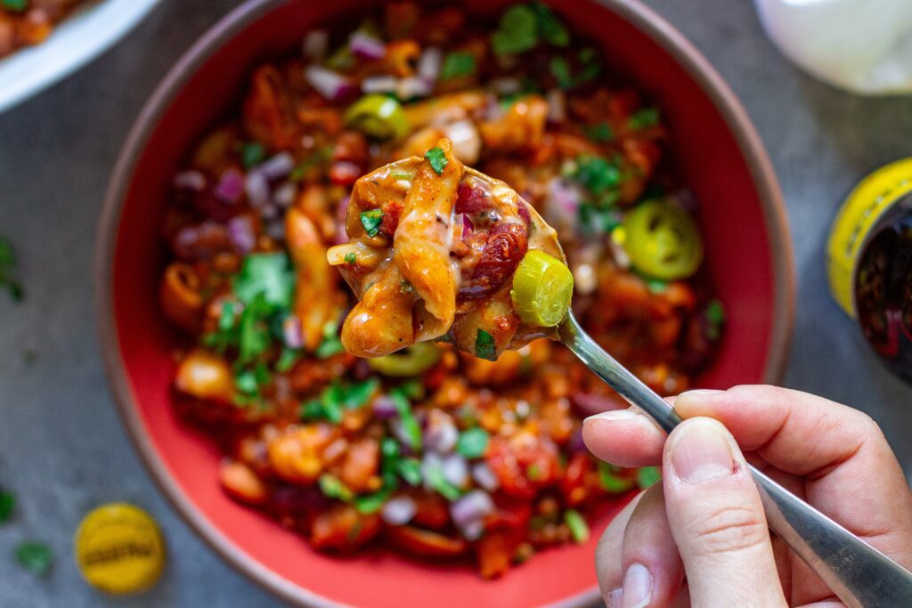 A bowl of cheesy and hearty One-Pot Lentil Chili Mac topped with fresh cilantro, red onion, pickled jalapeño, and vegan sour cream.