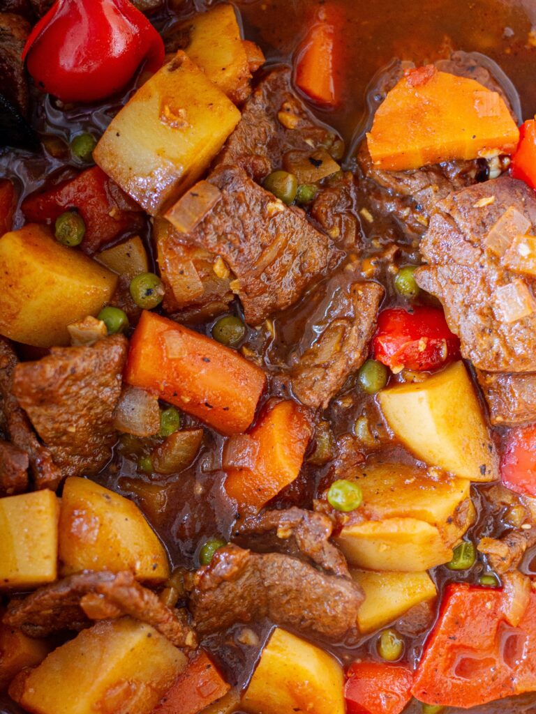 A close-up of tender vegan beef slices simmered in rich tomato sauce with carrots, potatoes, bell pepper, and peas.