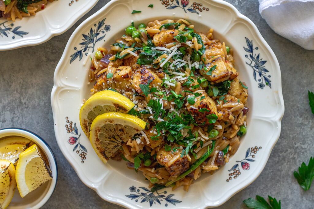 A plate of creamy lemon pepper tofu and orzo topped with vegan parmesan and parsley.