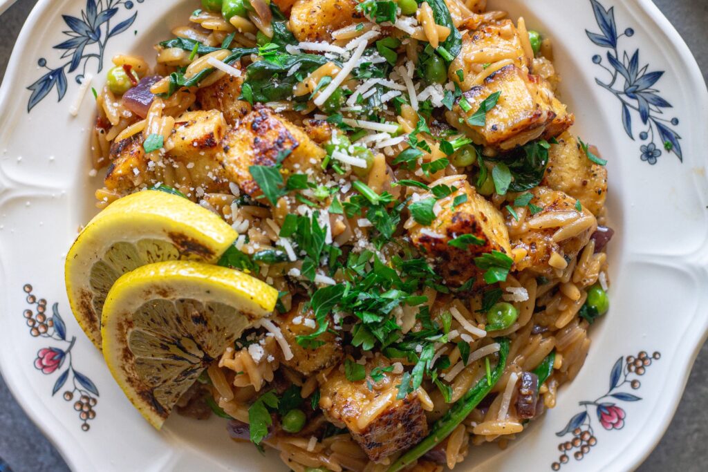 A plate of creamy lemon pepper tofu and orzo topped with vegan parmesan and parsley.