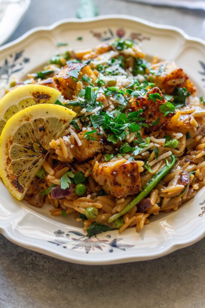 A plate of creamy lemon pepper tofu and orzo topped with vegan parmesan and parsley.