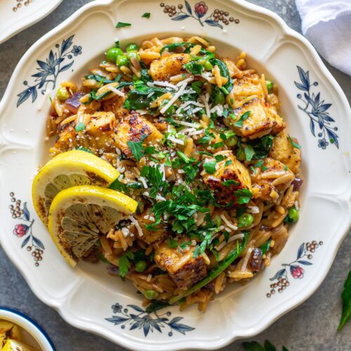 A plate of creamy lemon pepper tofu and orzo topped with vegan parmesan and parsley.