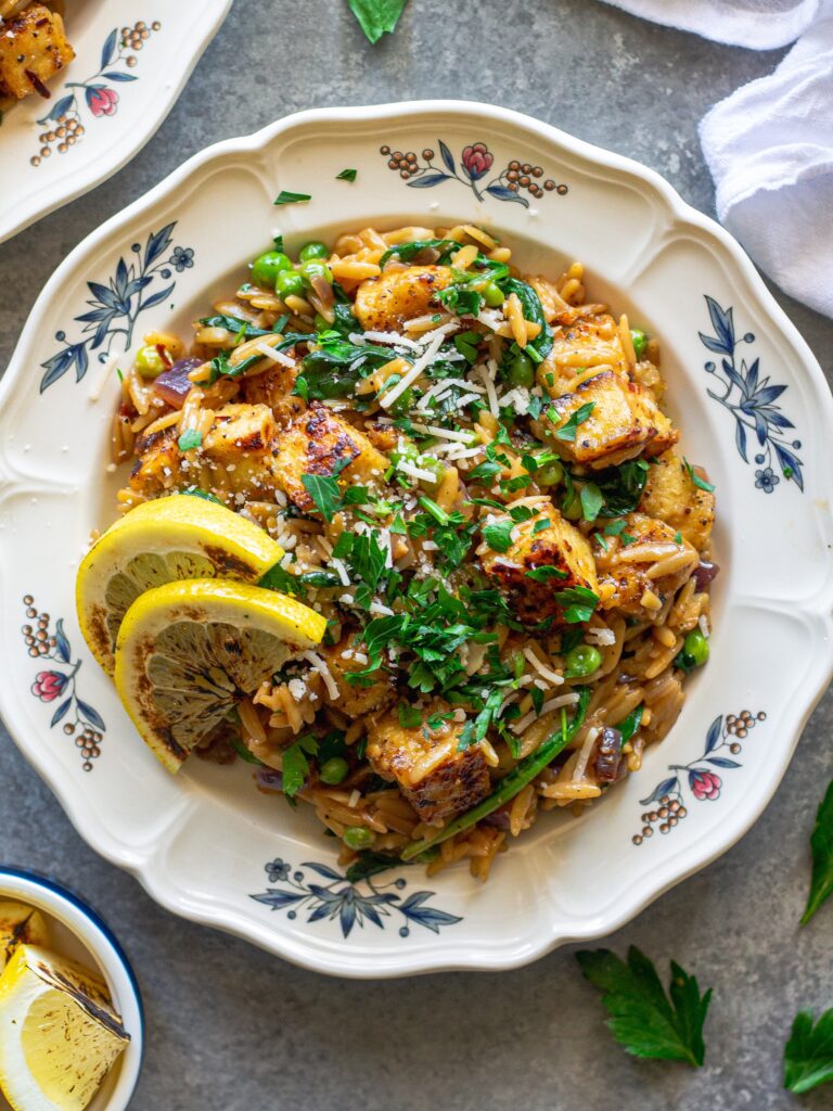 A plate of creamy lemon pepper tofu and orzo topped with vegan parmesan and parsley.