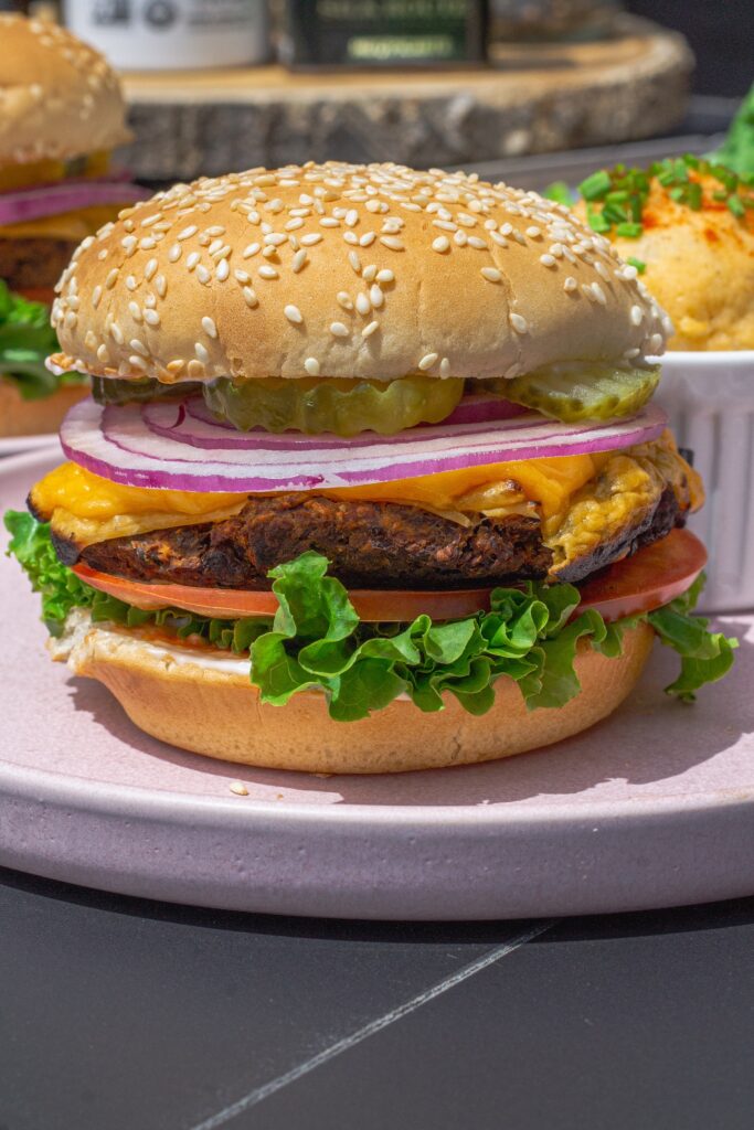 Close-up of a grilled black bean mushroom burger stacked with lettuce, tomato, onions and vegan cheese on a toasted bun