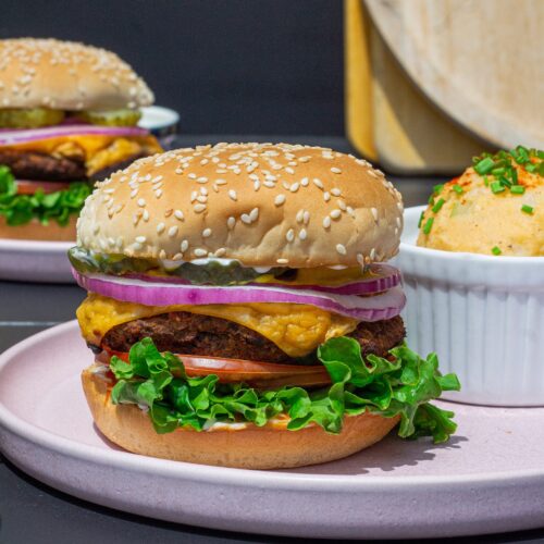 Close-up of a grilled black bean mushroom burger stacked with lettuce, tomato, onions and vegan cheese on a toasted bun