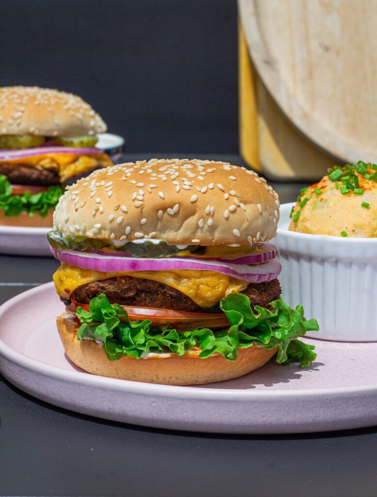 Close-up of a grilled black bean mushroom burger stacked with lettuce, tomato, onions and vegan cheese on a toasted bun