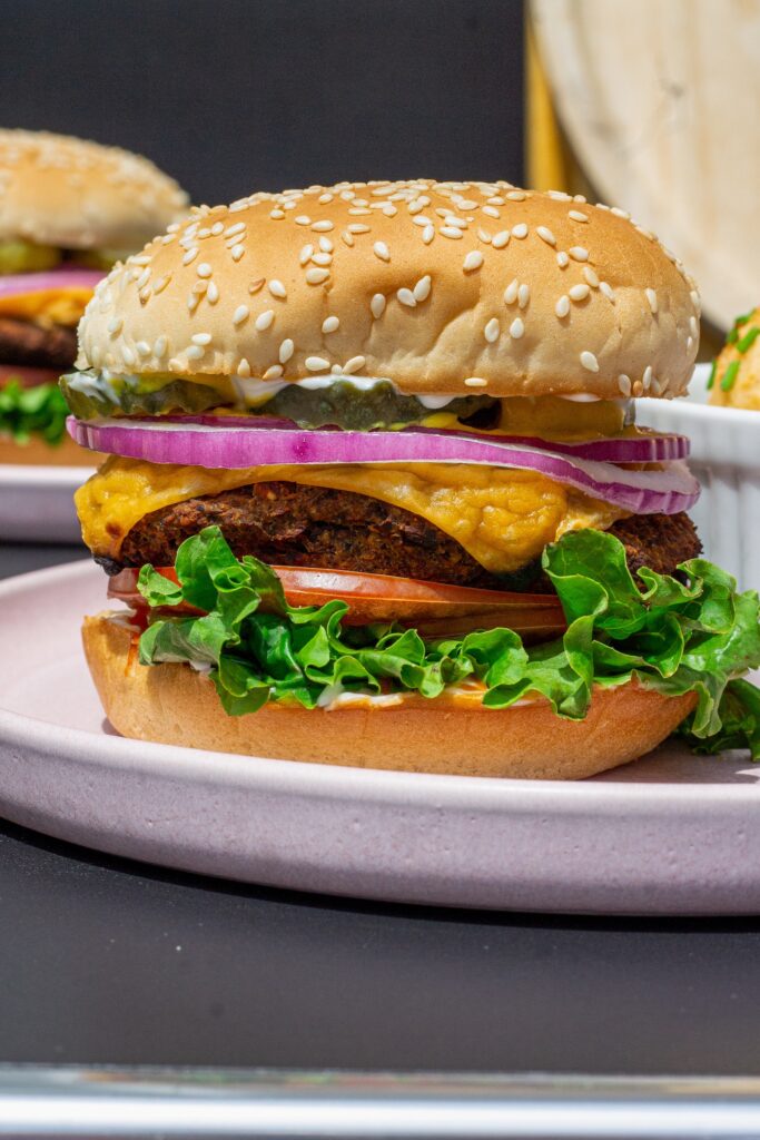 Close-up of a grilled black bean mushroom burger stacked with lettuce, tomato, onions and vegan cheese on a toasted bun