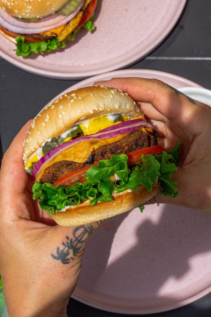 Close-up of a grilled black bean mushroom burger stacked with lettuce, tomato, onions and vegan cheese on a toasted bun