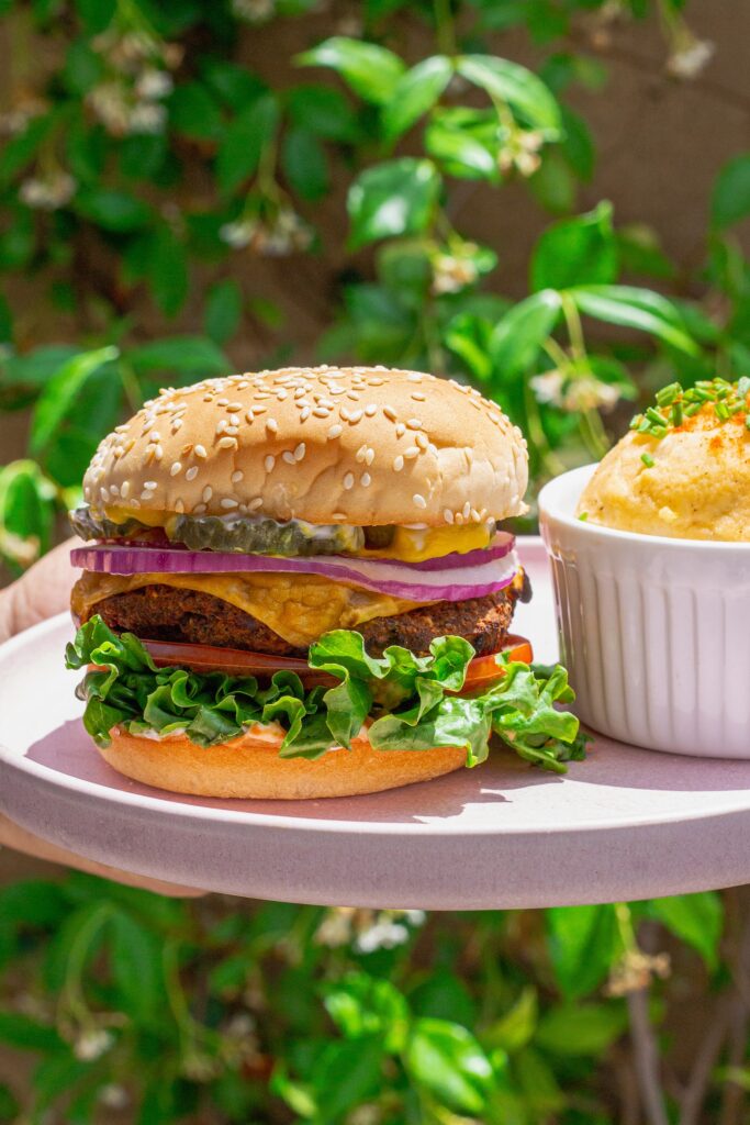 Close-up of a grilled black bean mushroom burger stacked with lettuce, tomato, onions and vegan cheese on a toasted bun