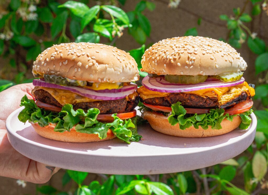 Close-up of a grilled black bean mushroom burger stacked with lettuce, tomato, onions and vegan cheese on a toasted bun