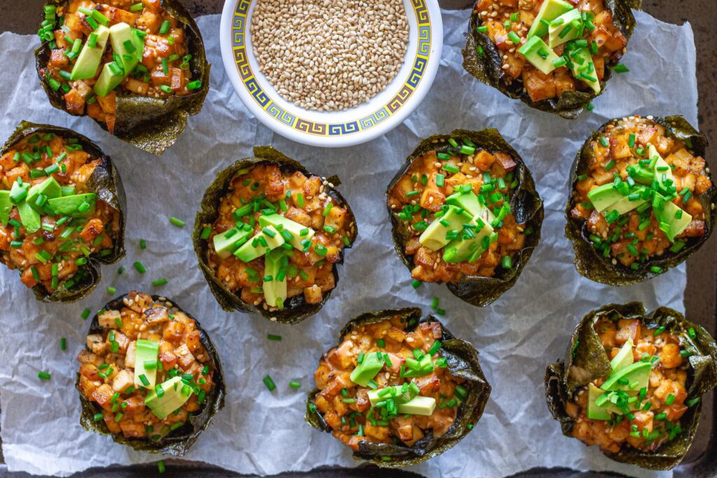 Vegan sushi bake cups garnished with avocado, green onion, and spicy mayo on a serving tray.