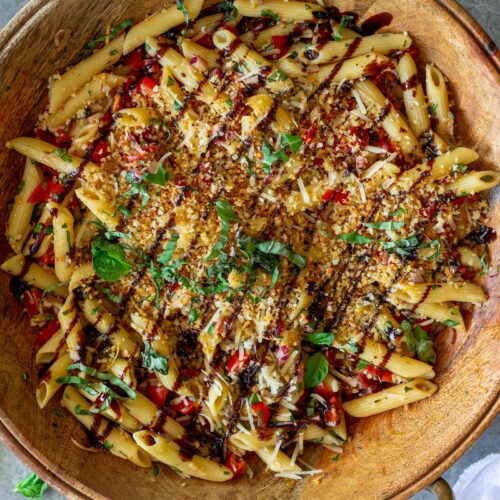 Overhead shot of bruschetta-inspired pasta salad in a serving bowl drizzled with balsamic glaze and garnished with basil and garlicky breadcrumbs.
