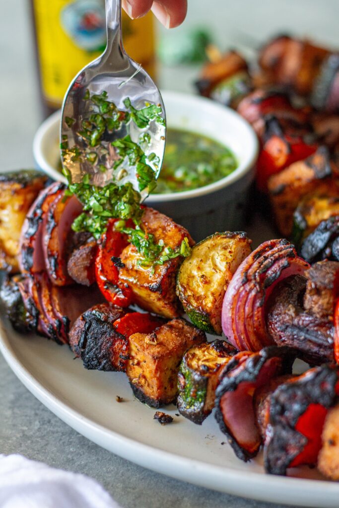 Finished skewers on a platter with a side of vibrant green chimichurri sauce.