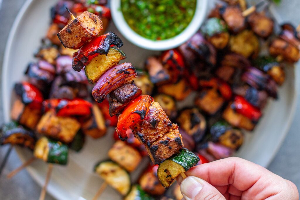 Finished skewers with chimichurri on a platter, with a side of vibrant green chimichurri sauce.