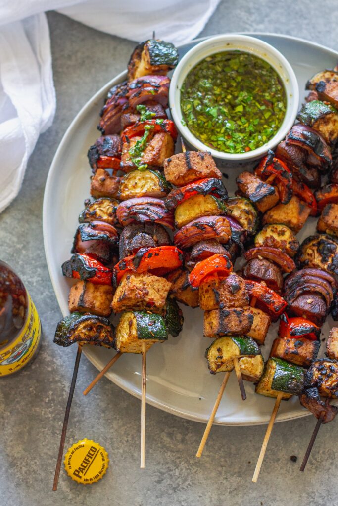 Finished skewers on a platter with a side of vibrant green chimichurri sauce.