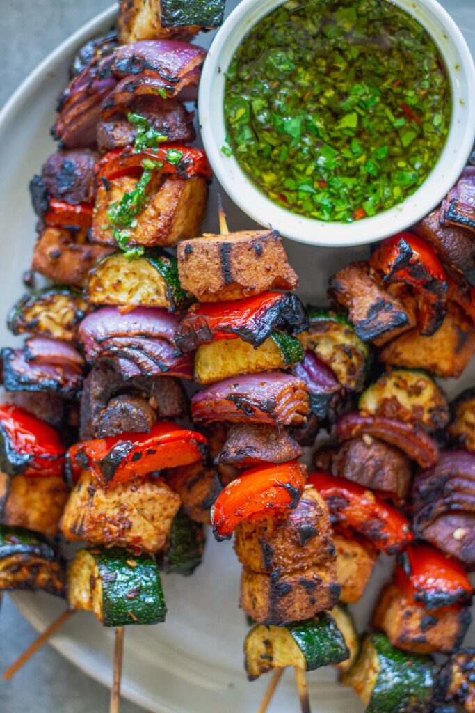 Finished skewers with chimichurri on a platter, with a side of vibrant green chimichurri sauce.