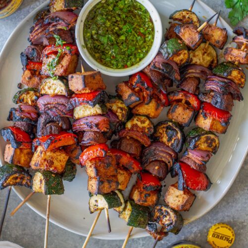 Finished skewers on a platter with a side of vibrant green chimichurri sauce.