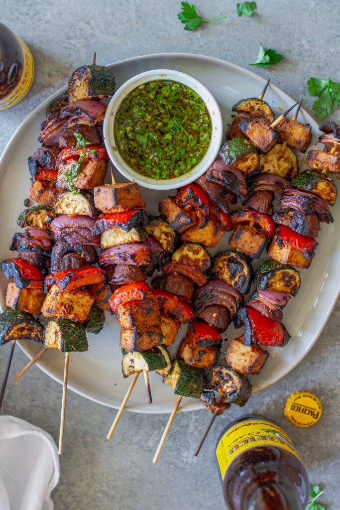 Finished skewers on a platter with a side of vibrant green chimichurri sauce.