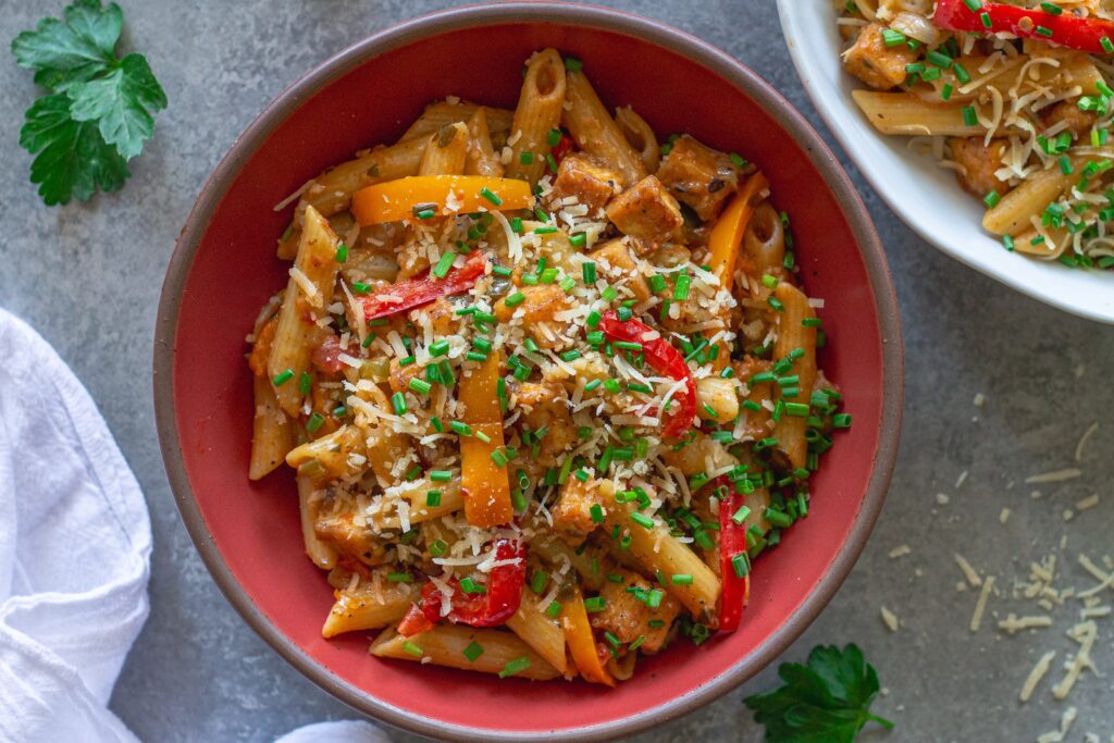 Bowl of Creamy One Pan Cajun-Inspired Pasta topped with chives and extra vegan parmesan.