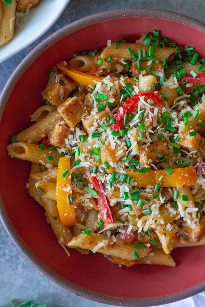 Bowl of Creamy One Pan Cajun-Inspired Pasta topped with chives and extra vegan parmesan.