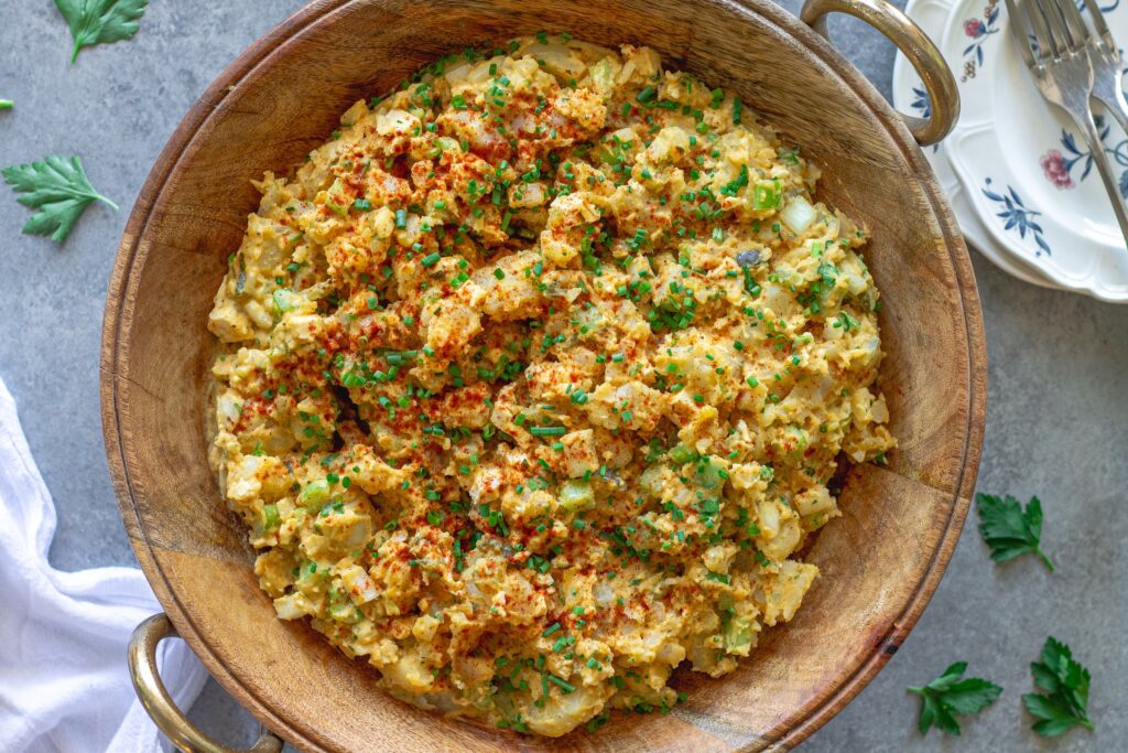 Overhead shot of creamy vegan Southern-style potato salad in serving bowl garnished with smoked paprika and chives