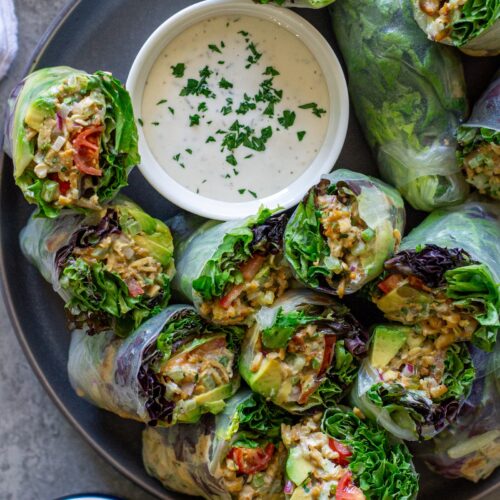 Chicken salad summer rolls sliced in half and arranged on a serving plate with a side of ranch dressing.