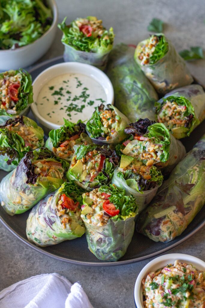 Chicken salad summer rolls sliced in half and arranged on a serving plate with a side of ranch dressing.