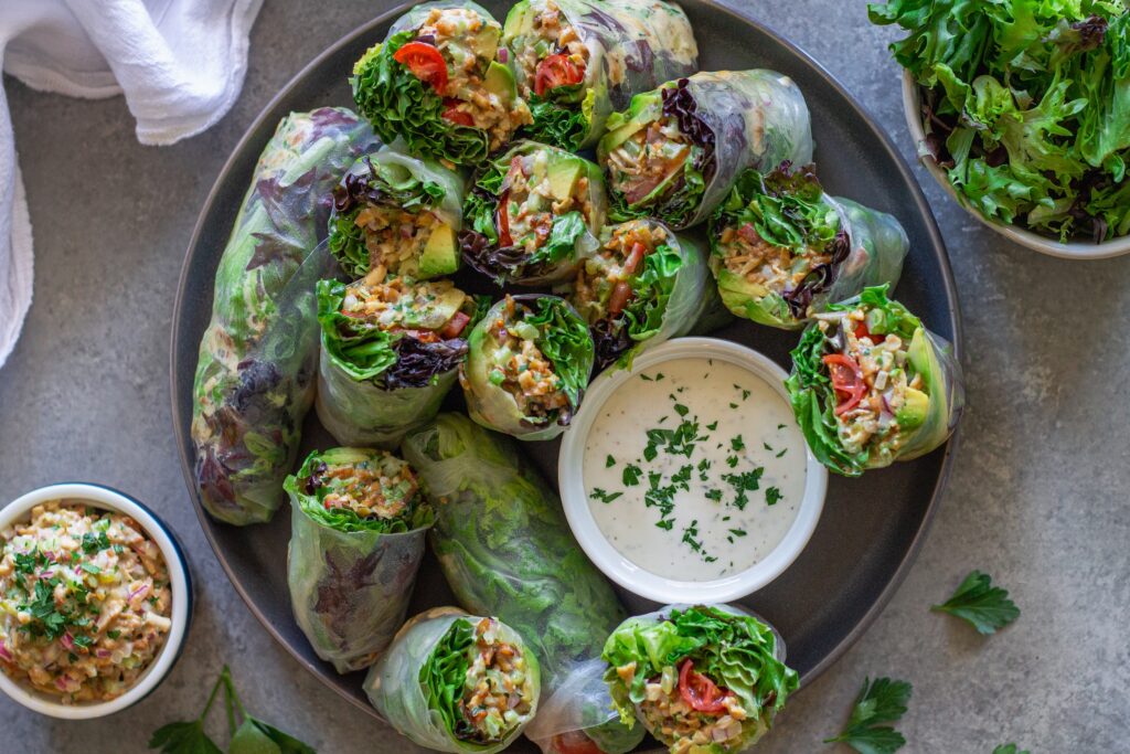 Chicken salad summer rolls sliced in half and arranged on a serving plate with a side of ranch dressing.