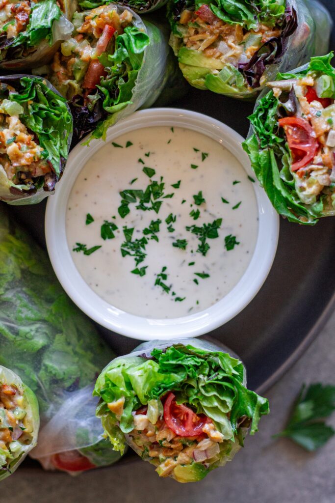 Chicken salad summer rolls sliced in half and arranged on a serving plate with a side of ranch dressing.