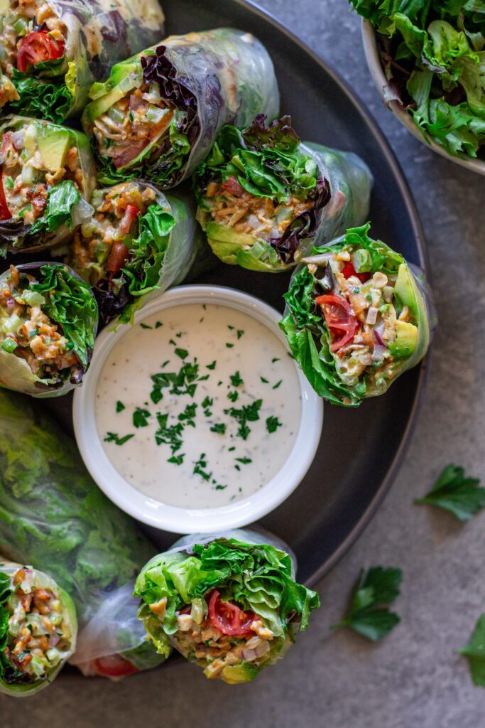Chicken salad summer rolls sliced in half and arranged on a serving plate with a side of ranch dressing.