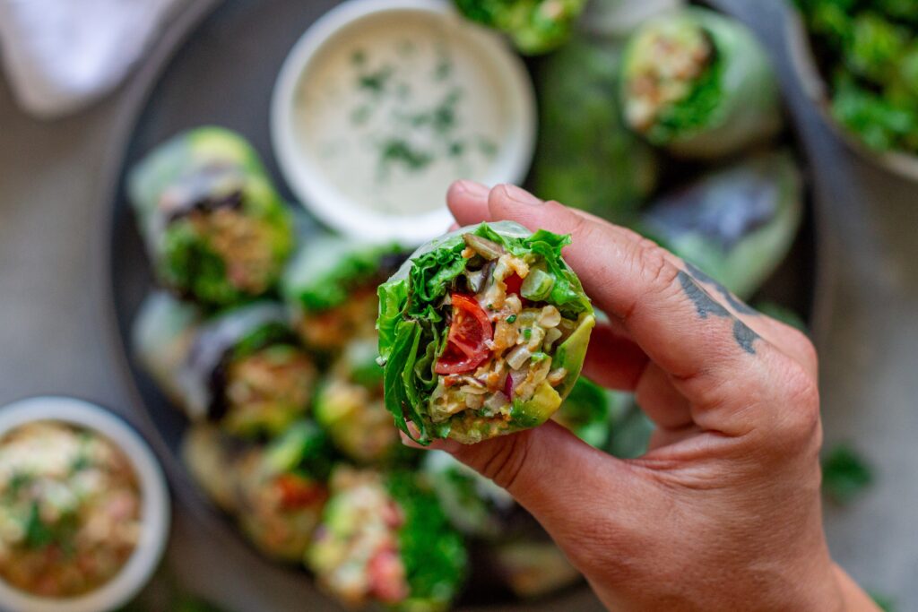Close-up of one chicken salad summer roll cut in half , showing detailed cross-section of tofu chicken salad, avocado, tomato, and lettuce.
