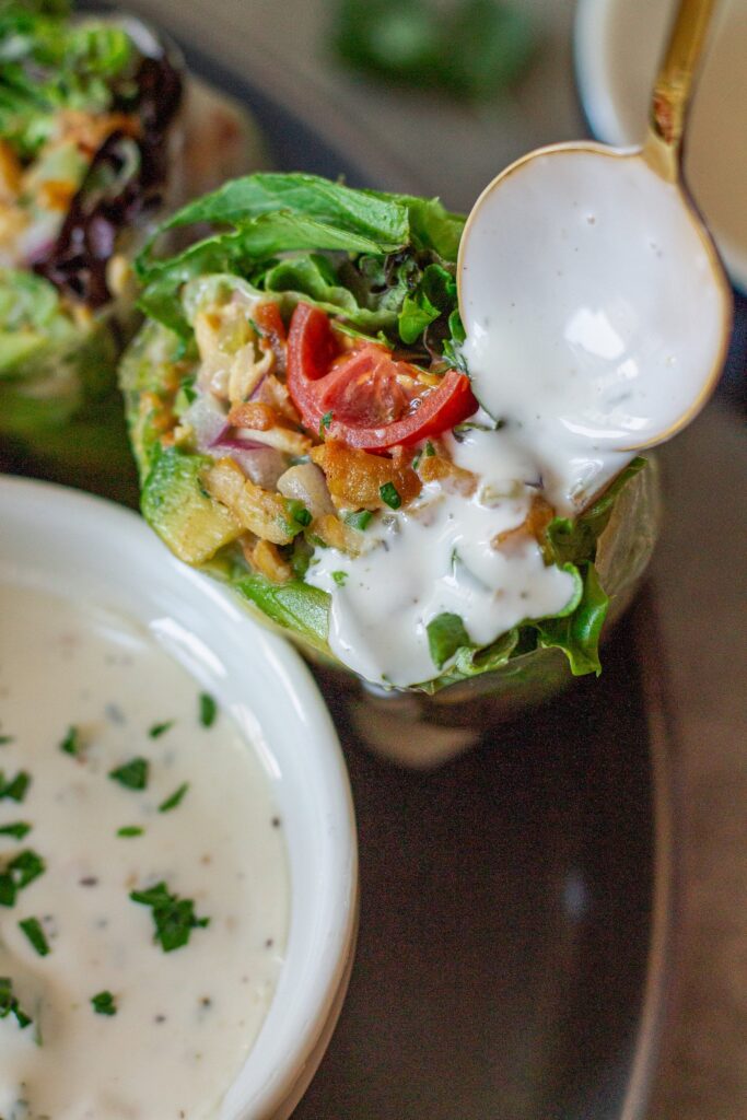 Close-up of one chicken salad summer roll cut in half , showing detailed cross-section of tofu chicken salad, avocado, tomato, and lettuce drizzled with ranch.