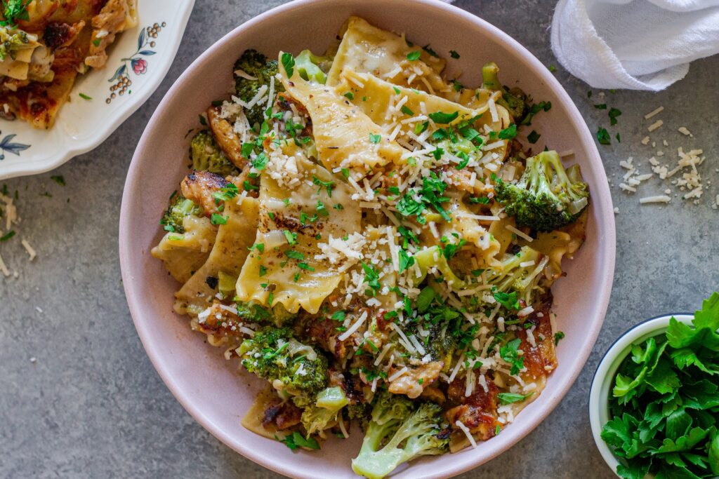 Overhead shot of creamy chicken and broccoli skillet lasagna on a plate, garnished with fresh parsley and vegan parmesan.