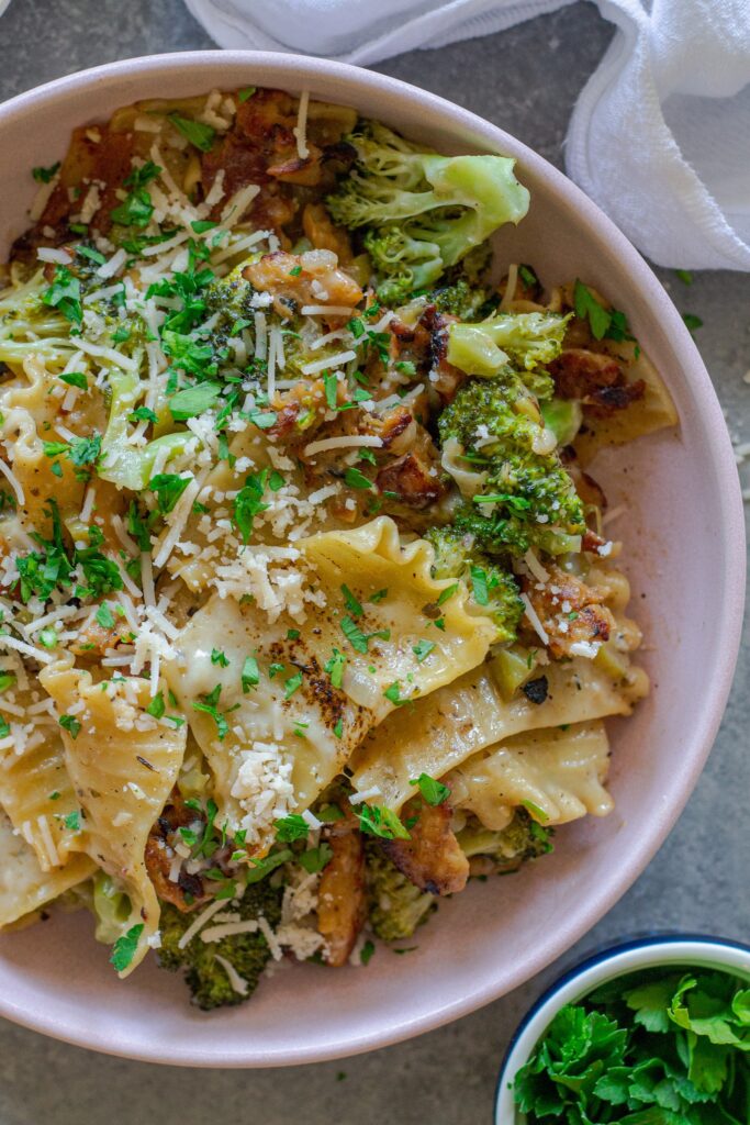 Overhead shot of creamy chicken and broccoli skillet lasagna on a plate, garnished with fresh parsley and vegan parmesan.