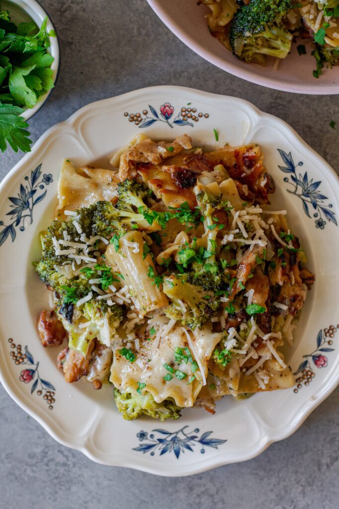 Overhead shot of creamy chicken and broccoli skillet lasagna on a plate, garnished with fresh parsley and vegan parmesan.