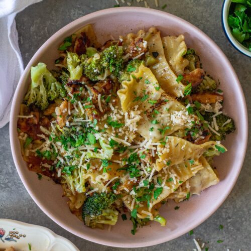 Overhead shot of creamy chicken and broccoli skillet lasagna on a plate, garnished with fresh parsley and vegan parmesan.