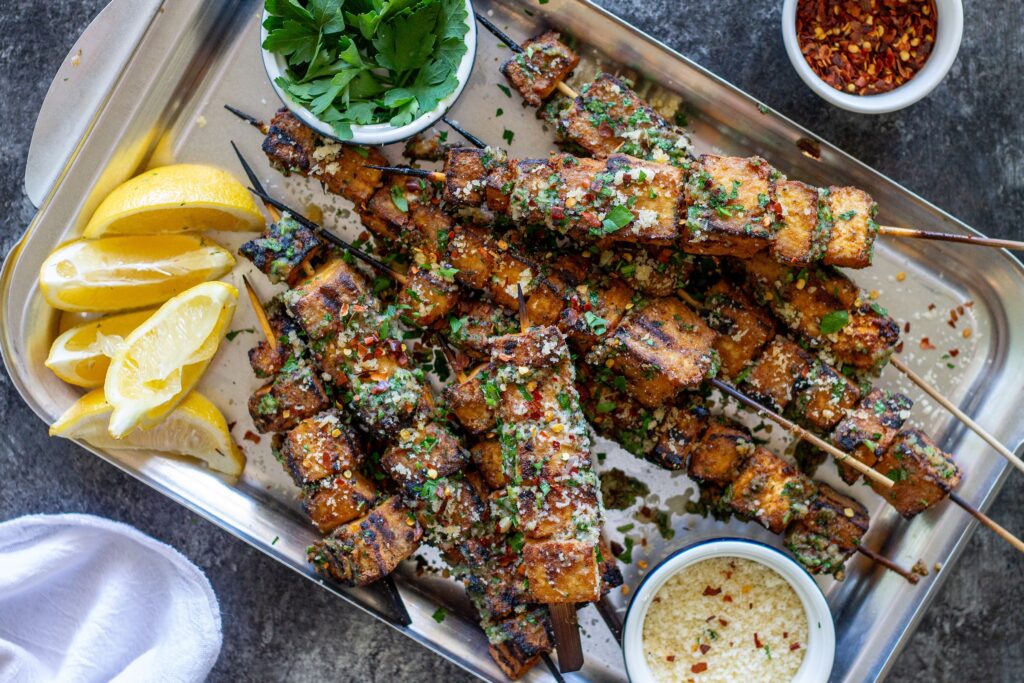 Garlic parmesan tofu skewers brushed with garlic parmesan butter and garnished with parsley, red chili flakes, and grated parmesan.