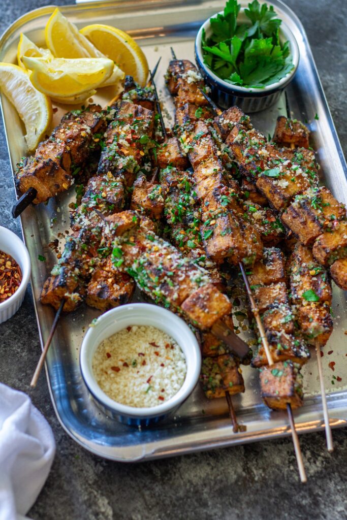 Garlic parmesan tofu skewers brushed with garlic parmesan butter and garnished with parsley, red chili flakes, and grated parmesan.