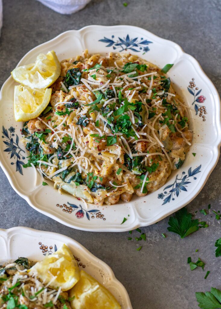 Overhead shot of lemon pesto orzo and chickpeas on a serving plate garnished with fresh parsley and vegan parmesan.