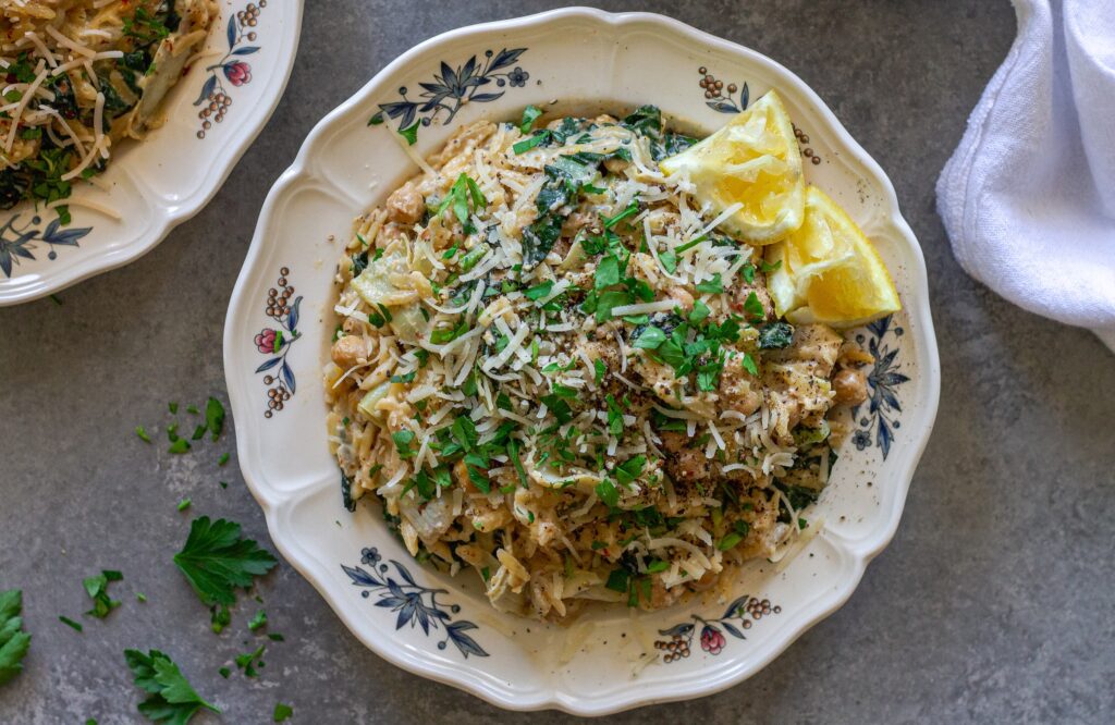 Overhead shot of lemon pesto orzo and chickpeas on a serving plate garnished with fresh parsley and vegan parmesan.