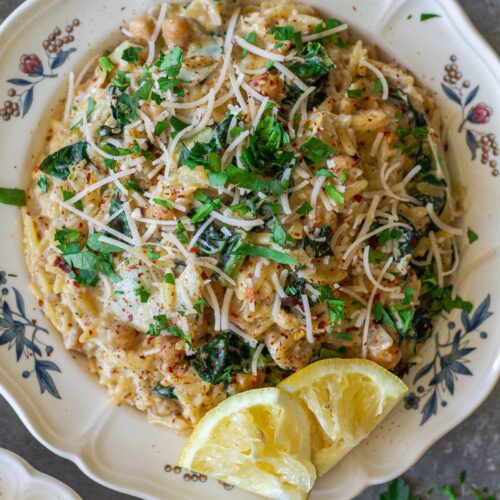 Overhead shot of lemon pesto orzo and chickpeas on a serving plate garnished with fresh parsley and vegan parmesan.