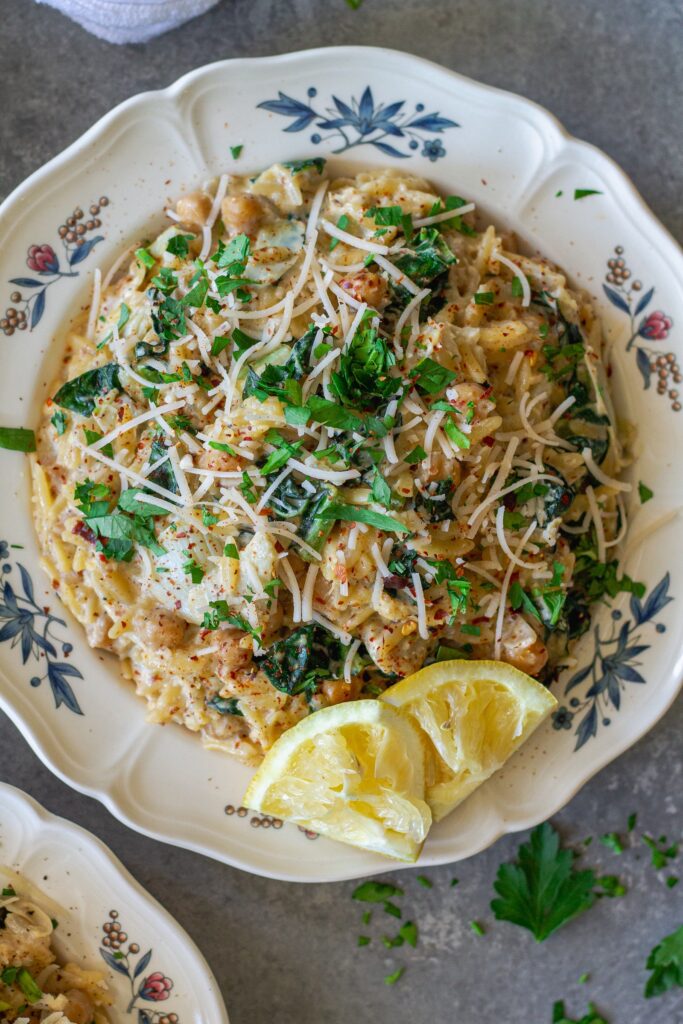Overhead shot of lemon pesto orzo and chickpeas on a serving plate garnished with fresh parsley and vegan parmesan.