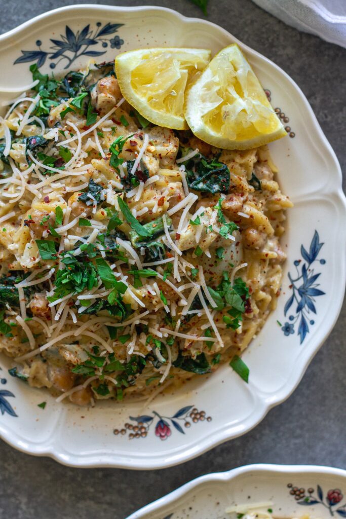 Overhead shot of lemon pesto orzo and chickpeas on a serving plate garnished with fresh parsley and vegan parmesan.